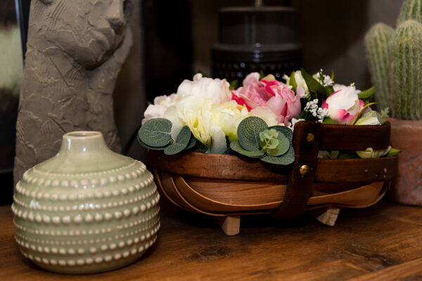 Basket of pink and white peonies on a dresser, next to round art deco vase and small cactus plant