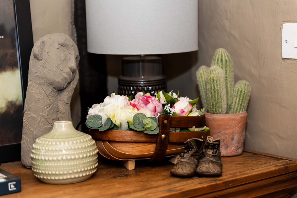 Home decor arrangements with female head sculpture, round vase, small cactus, tiny vintage baby shoes and a pretty basket of pink and white peonies