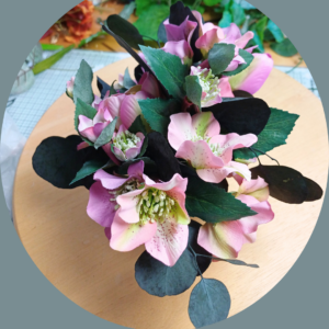 Pink and mauve hellebore flowers in a small arrangement on a round wooden platform