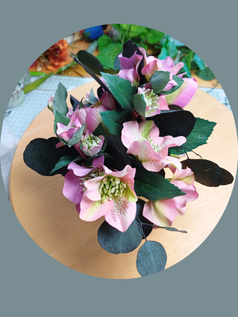 Pink and mauve hellebore flowers in a small arrangement on a round wooden platform