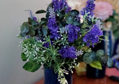 Silk lavender spears arranged in a blue ceramic vase with preserved eucalyptus and faux white wax flowers