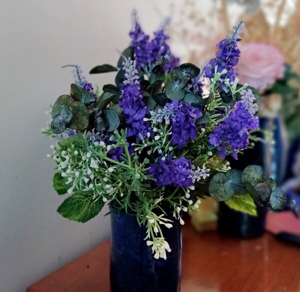 Silk lavender spears arranged in a blue ceramic vase with preserved eucalyptus and faux white wax flowers