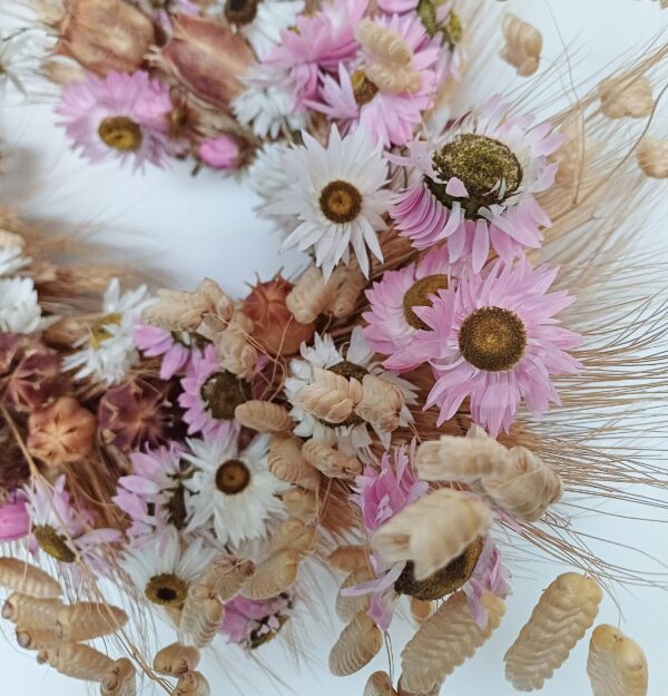 Close up image of heart shaped wreath with dried grasses and pink and white dried flowers