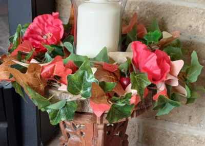 Image of table centre with green, read and brown ivy leaves, with two large red silk poppies. There is a large white pillar candle in the middle