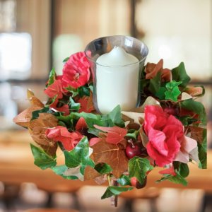 Image of table centre with green, read and brown ivy leaves, with two large red silk poppies. There is a large white pillar candle in the middle