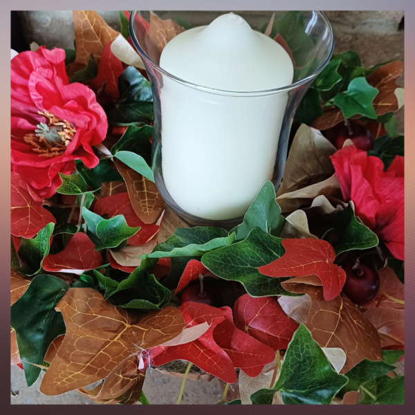 Image of table centre with green, read and brown ivy leaves, with two large red silk poppies. There is a large white pillar candle in the middle