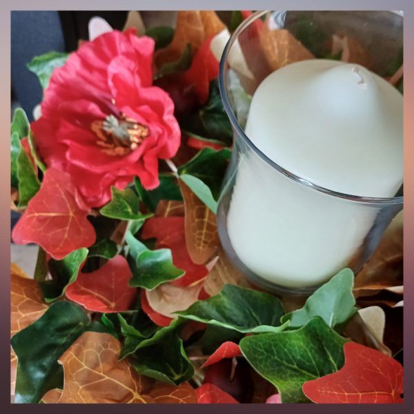 Image of table centre with green, read and brown ivy leaves, with two large red silk poppies. There is a large white pillar candle in the middle