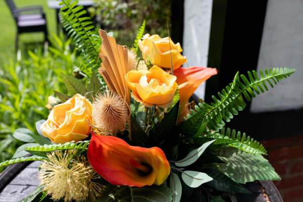 table arrangement with deep orange faux calla lilies, orange silk roses and faux ferns and foliage