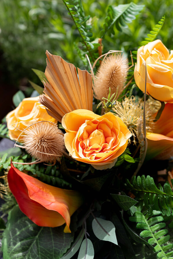 Close up image of sunshine glow table centre, with orange roses, calla lilies and dried palm leaf