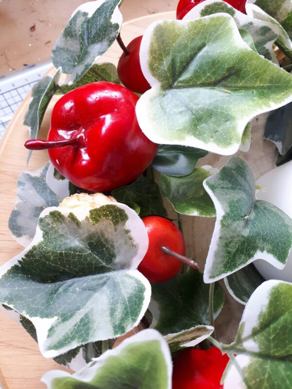 Detail of variegated ivy, red apples and mini bleached pine cones in a festive table centre