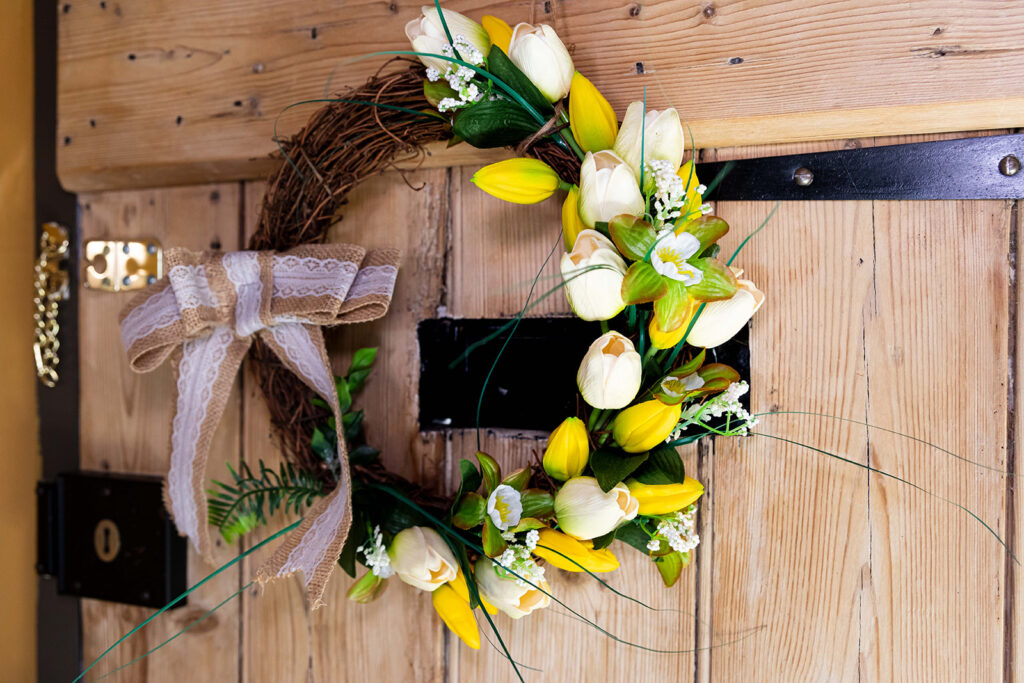 Image of a wreath of faux yellow and white tulips, hanging on the inside of a front door.