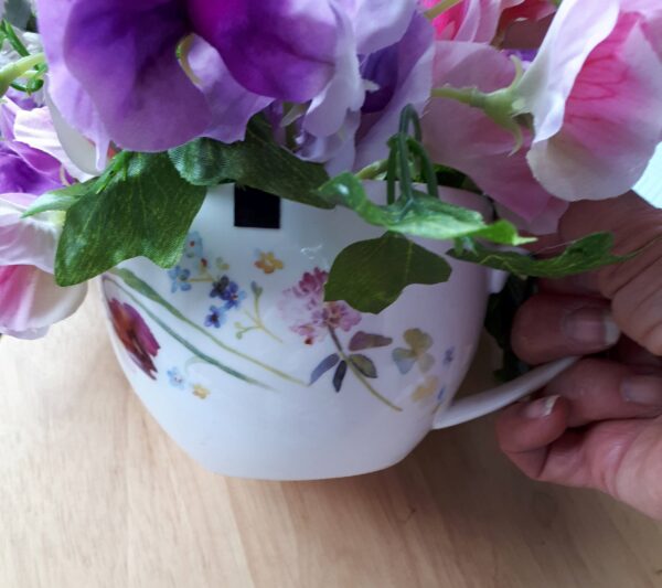 Image of pink and mauve sweet peas with pale pink fau alliums, in a pretty cup painted with little flowers