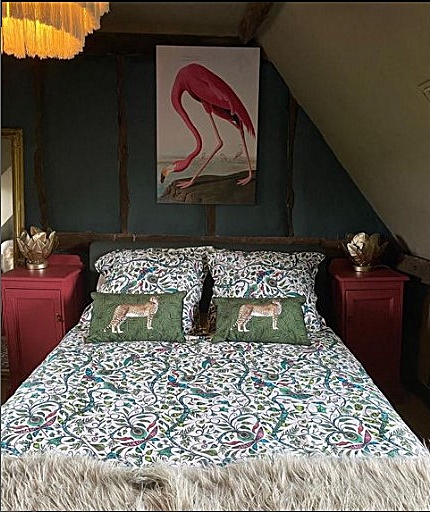 Image of small bedroom with double bed.  The bed cover has turquoise and purple pattern with birds.  Two matching occasional pillows feature cheetahs, and there is a large picture on the wall above the bed of a flamingo. 