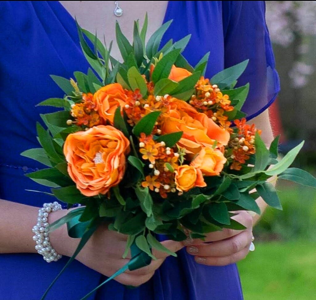 Image of bridesmaid's posy of orange silk flowers and deep green silk foliage
