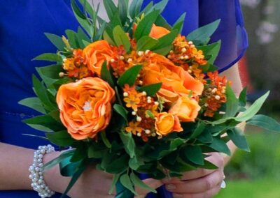 Image of bridesmaid posy. The flowers are orange silk roses with deep green silk foliage