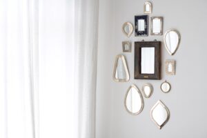 Image of wall with several small mirrors hung together.  They are all different shapes, some with gold frames, and one centre mirror has a wooden frame
