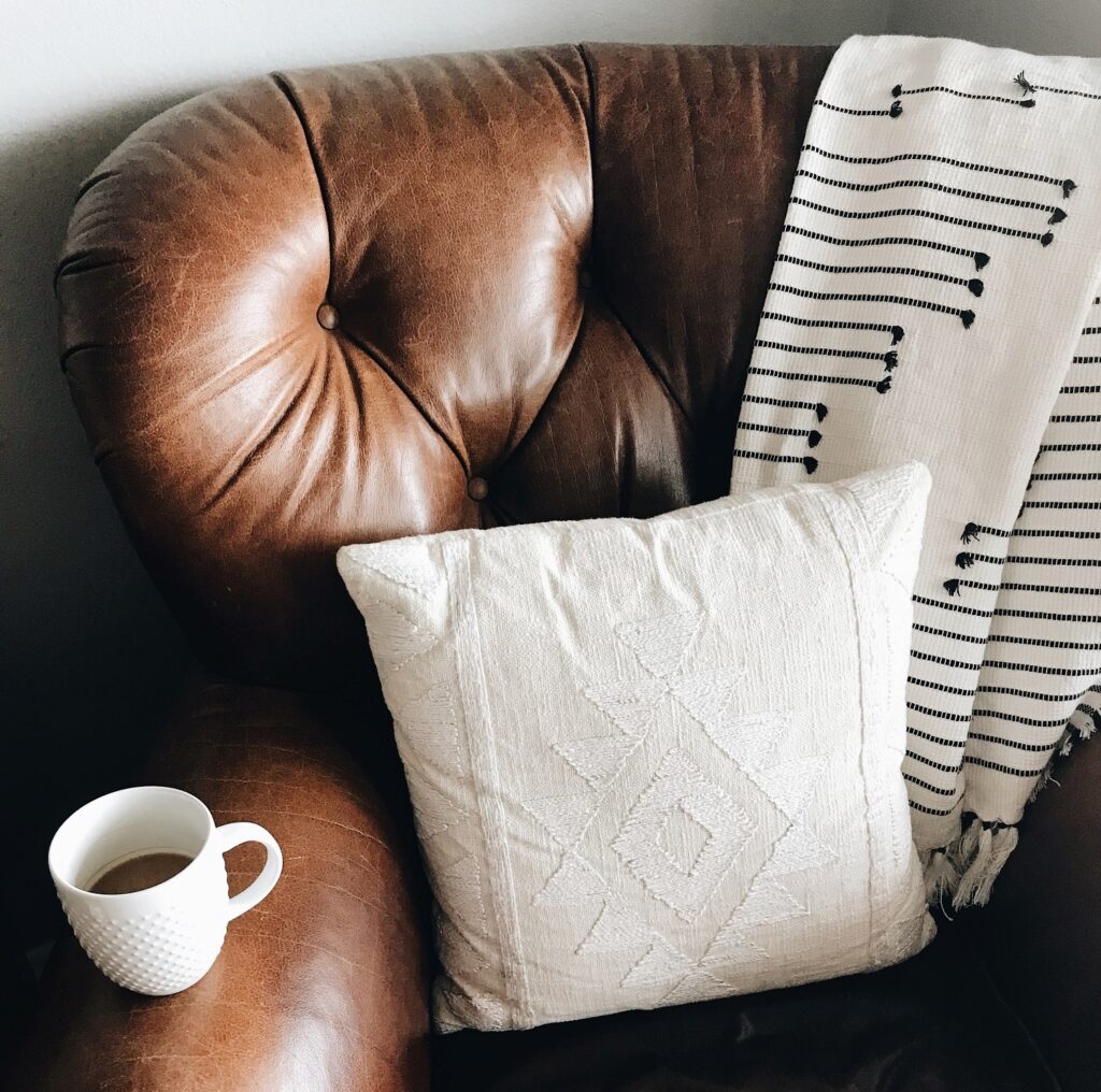 Imagae of chocolate brown leather chair, with a striped woollen throw, a cream cushion and a cup of coffee