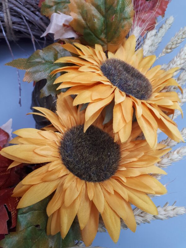 Close up photo of two silk sunflowers in a wreath. The colour is a rich yellow with a dark centre.