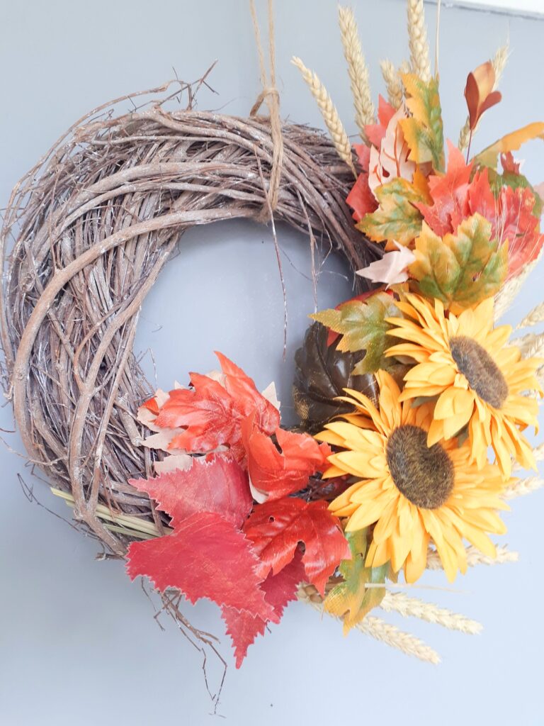 Image of an autumn sunflower wreath. Bright yellow sunflowers contrasted with autumn leaves, on a woven rattan wreath base