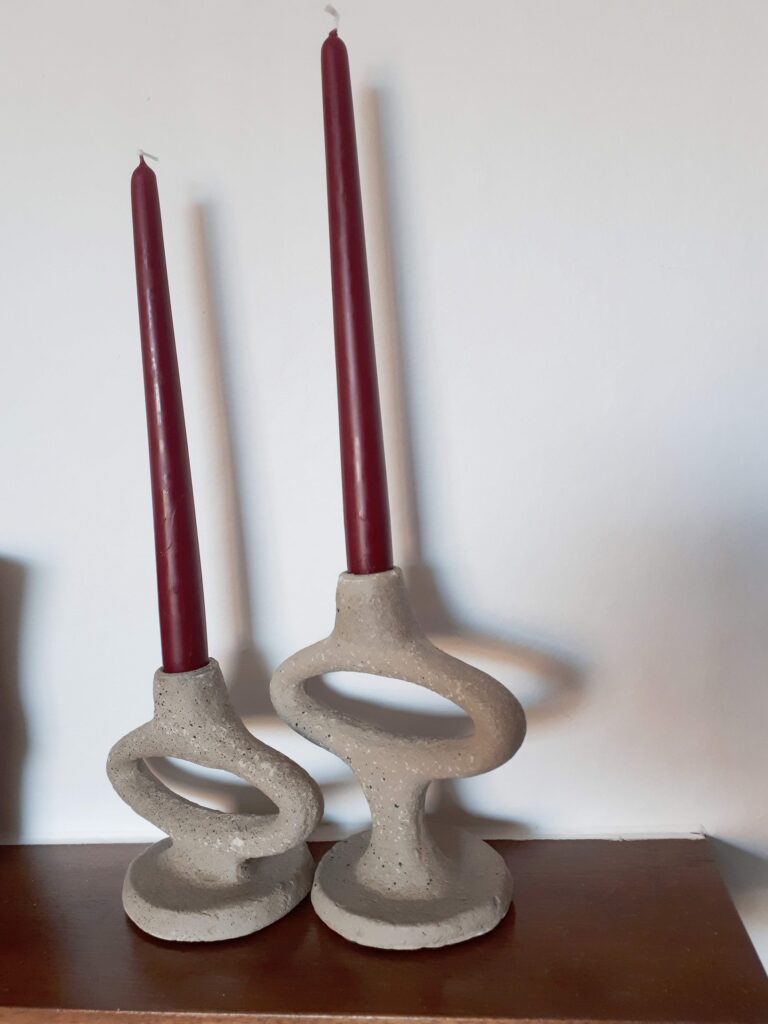 Image of two stoneware candlesticks with burgundy candles. The candlesticks have an oval design