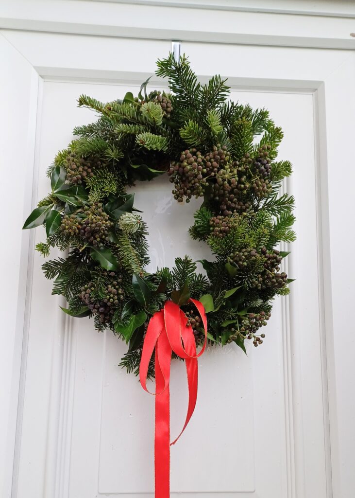 Image of door wreath made with natural folaige and ivy berries, and finished with a red bow and ribbon