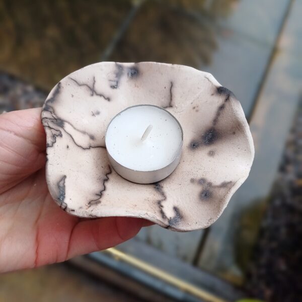 Ceramic tealight holder with tealight. The Holder is a a soft peach colour with a thred pattern, created using raku firing.