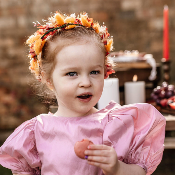 Image of little girl wearing a floral crown of deep orange silk flowers and orange bunnytail grasses