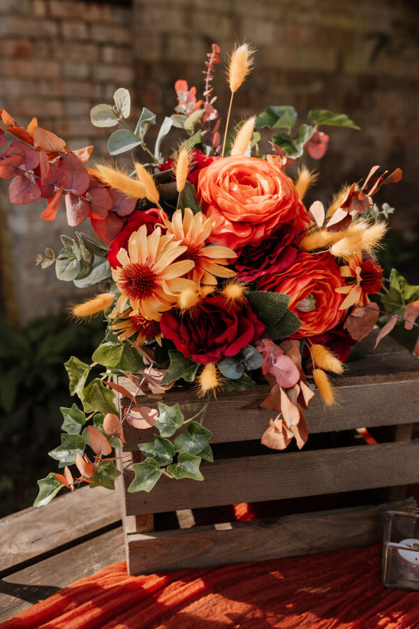 Image of bouquet of silk flowers in deep reds, orange and yellow.