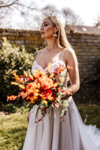 Image of bouquet of silk flowers in deep reds, orange and yellow. The bouquet is carried by a bride model