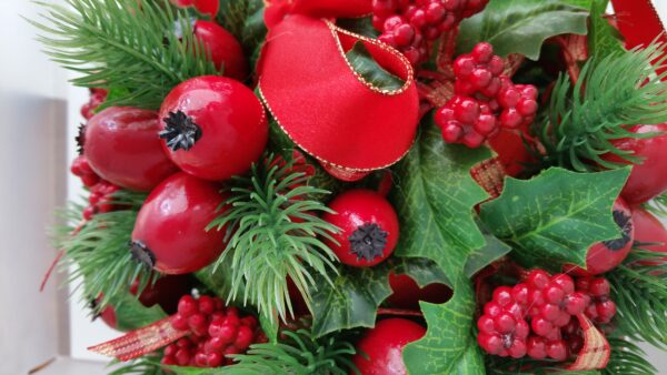 Details of ball of faux red berries and holly leaves, with red ribbon