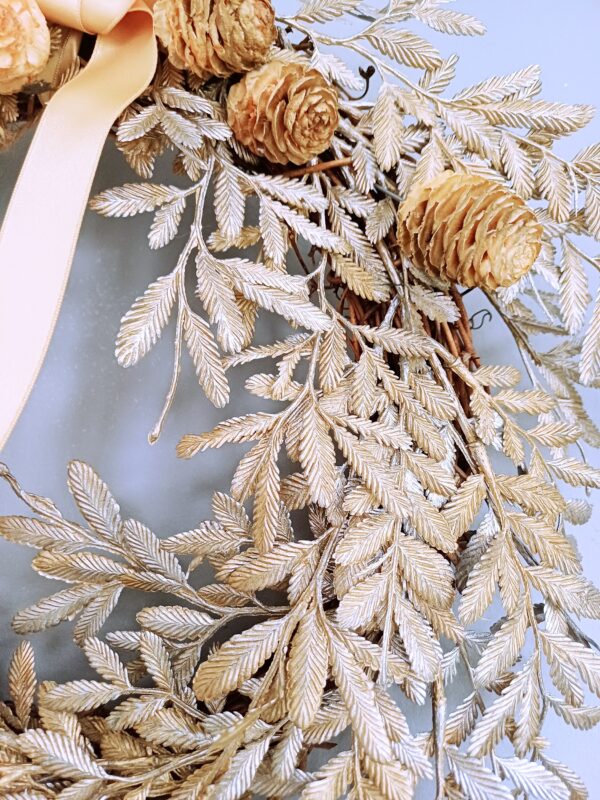 Close up image of gold leaf fronds and mini pinecones on a winter wreath