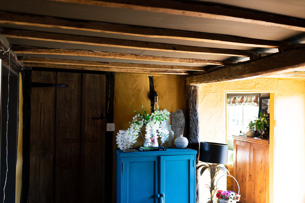 Image of a cottage room, decorated with honey brown walls, with a bright blue cupboard to add a pop of colour. Shows mindul maximalism.