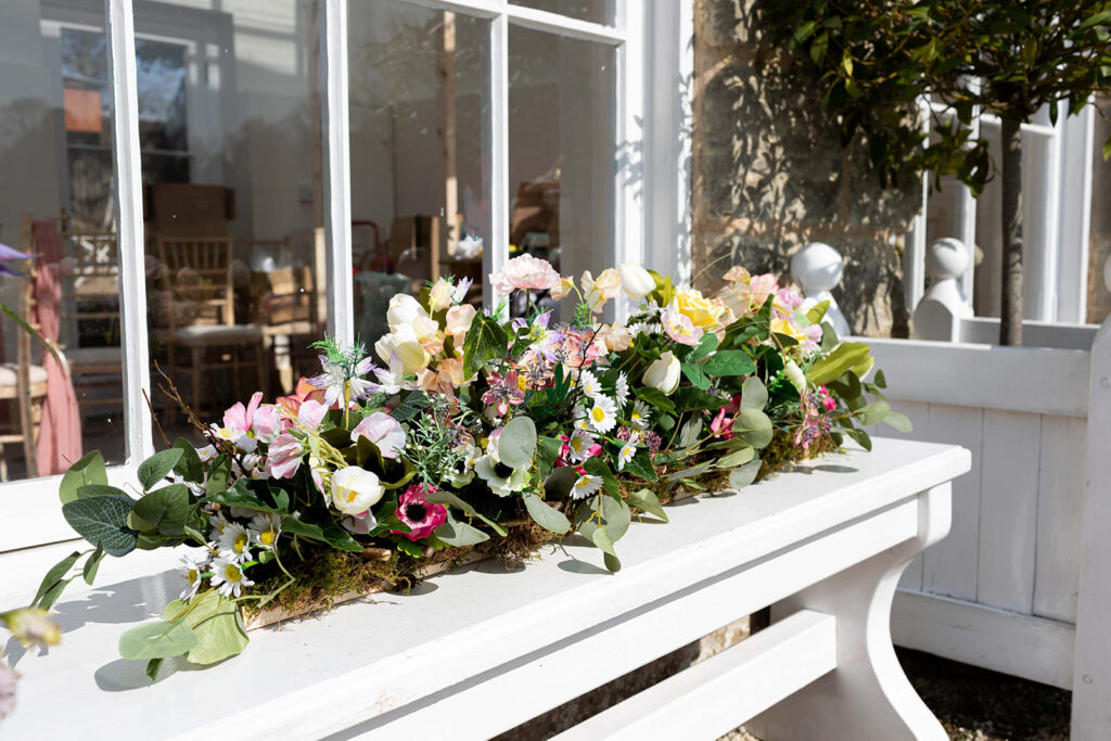 Spring silk flowers in a long arrangement on a wondowsill