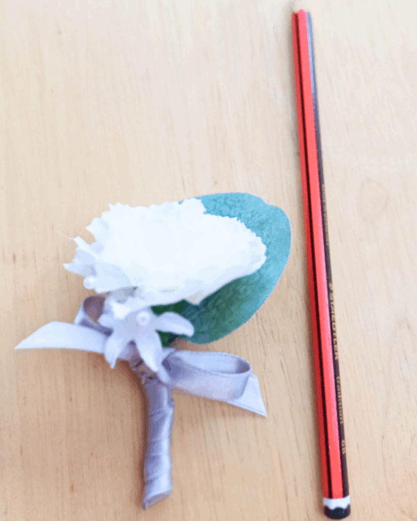 Image of pageboy mini buttonhole showing size detail (against a pencil) of carnation, silk baby's breath flower and silver satin bow.
