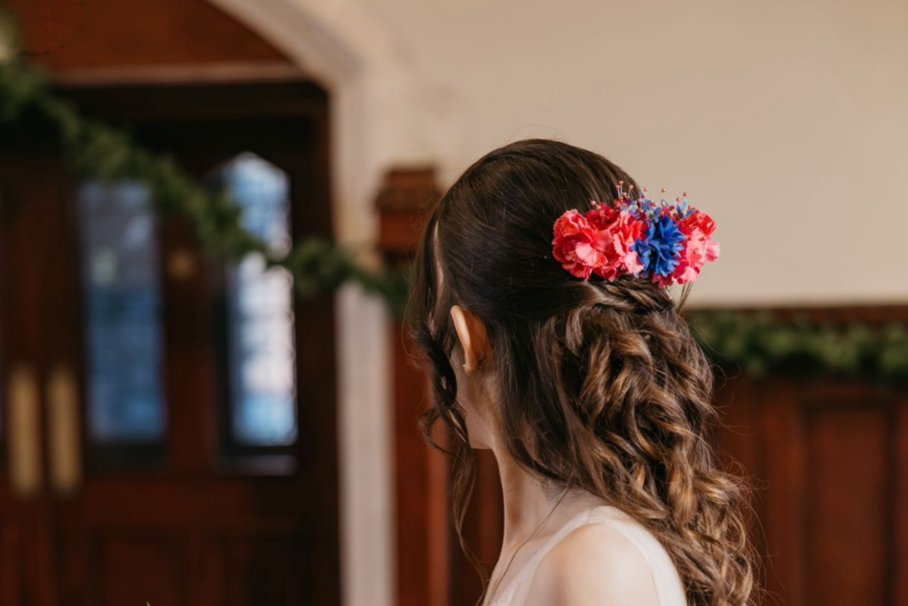 Image of bride showing her brown curls and flower comb pinned to the back of her head. Colours are bright pink and blue