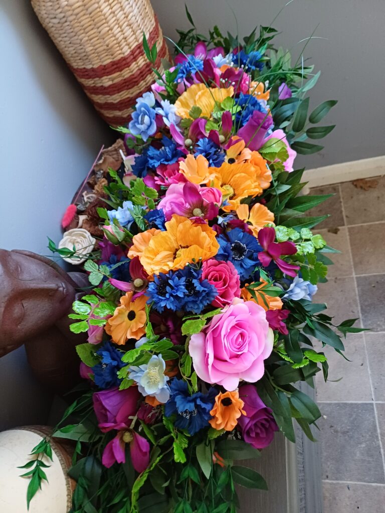 Image of table arrangement in bright silk flowers. Colours are orange, pink, blue and purple