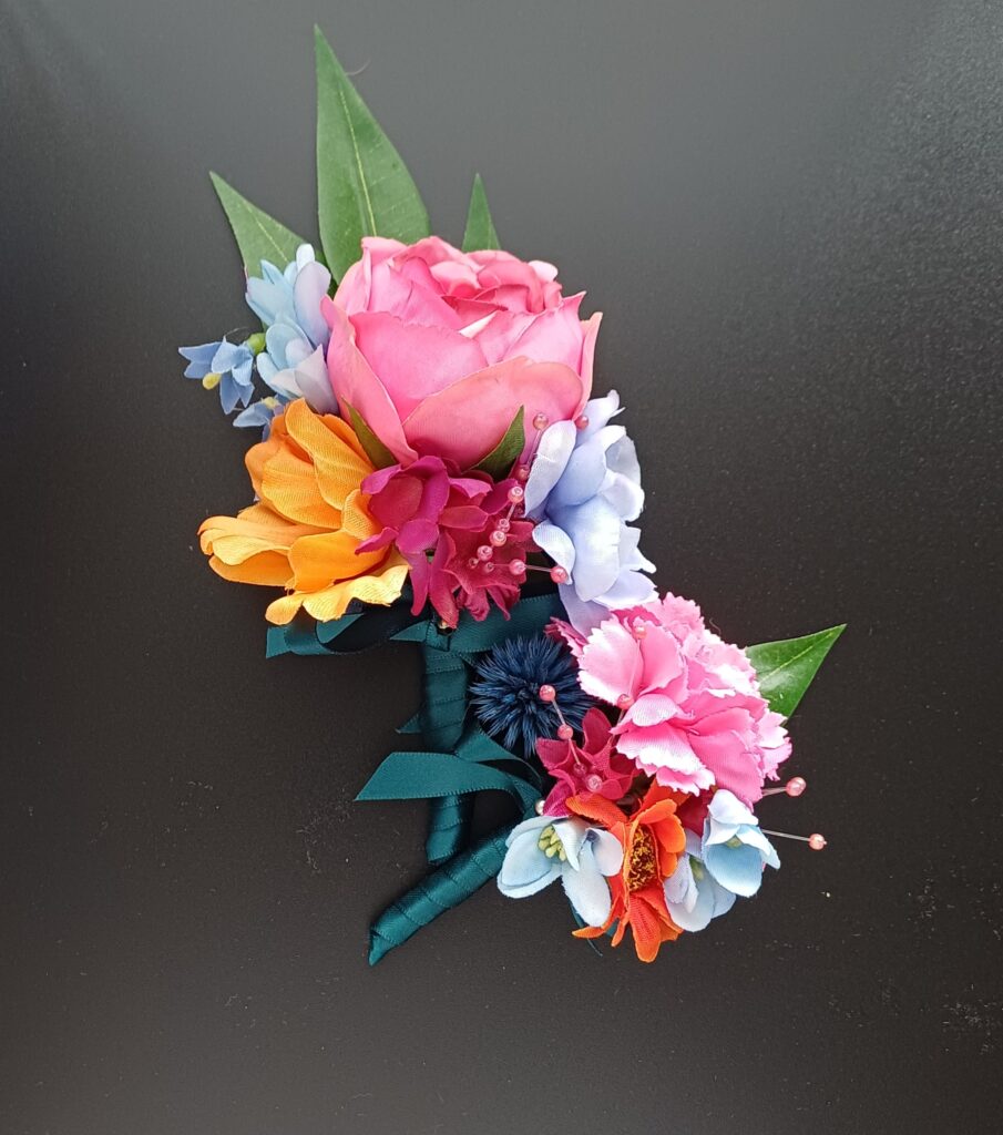 Groom's buttonhole and baby boy's buttonhole with bright flowers in pink, orange and pale blue