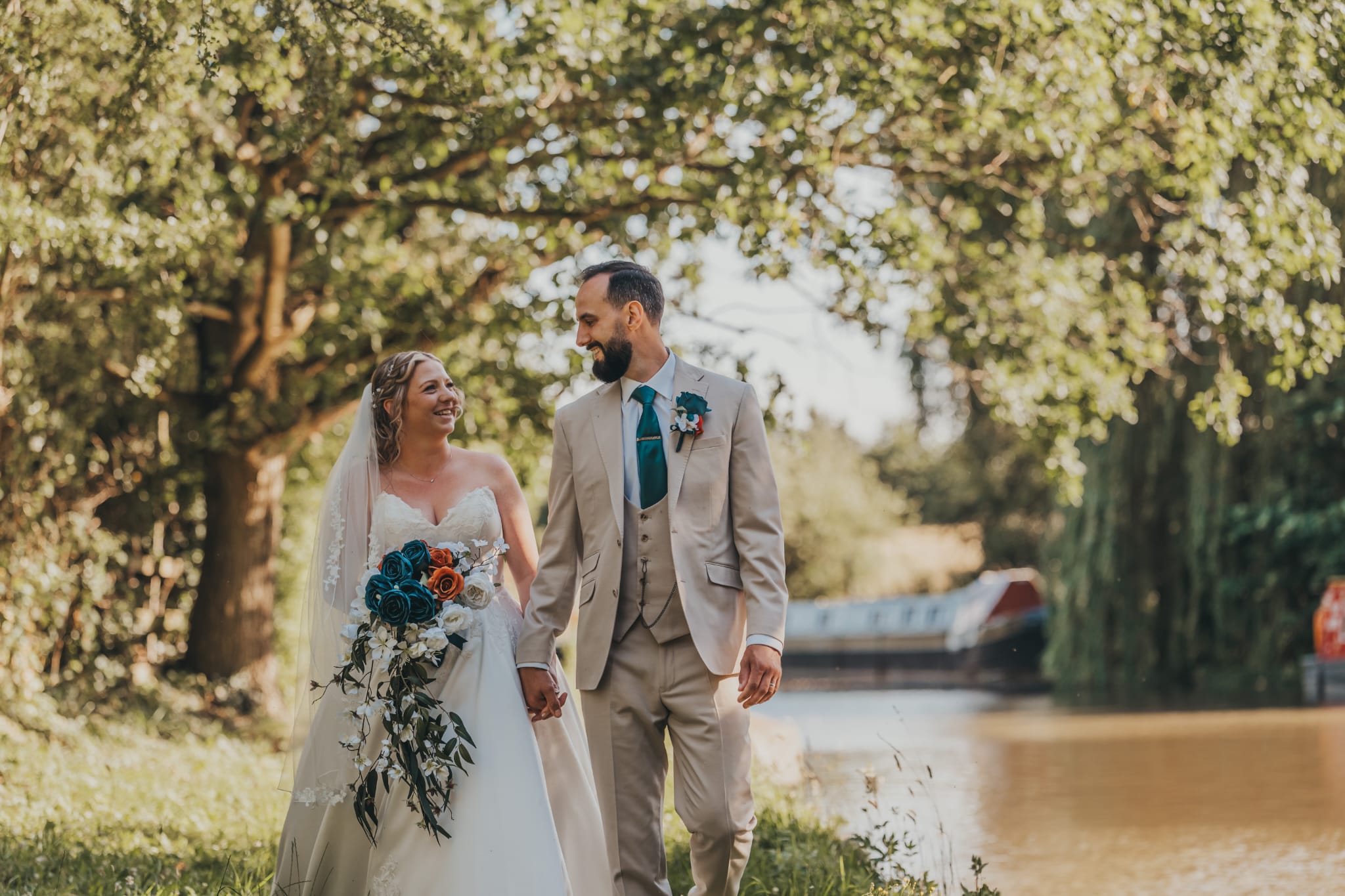 Wedding couple walking by the river with bride carrying her bouquet